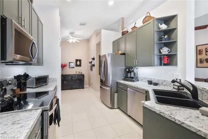 Kitchen featuring appliances with stainless steel finishes, light stone counters, sink, and ceiling fan