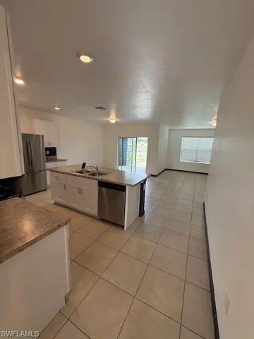 Kitchen featuring white cabinets, a kitchen island with sink, dishwashing machine, light tile patterned floors, and recessed lighting