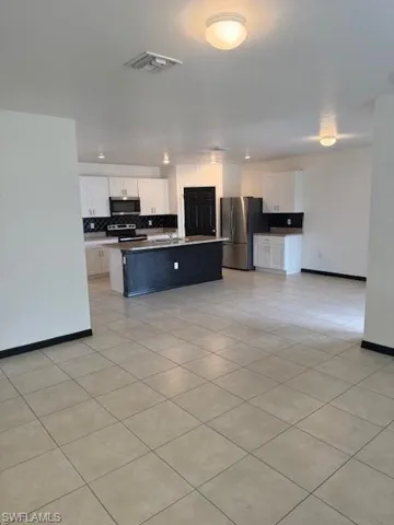 Kitchen featuring fridge, white cabinetry, a kitchen island with sink, and stainless steel range