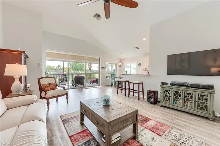 Living room featuring light wood finished floors, visible vents, ceiling fan, and vaulted ceiling