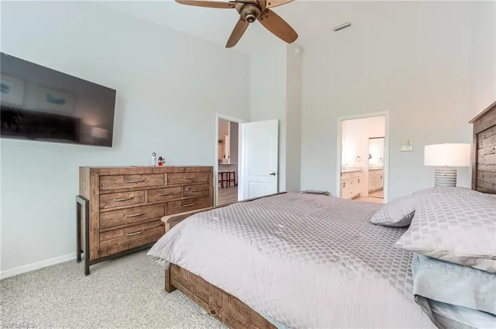 Bedroom with ensuite bathroom, baseboards, light colored carpet, visible vents, and a towering ceiling