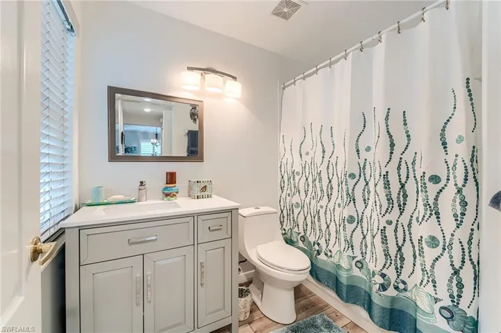 Bathroom with a shower with curtain, vanity, toilet, visible vents, and wood finished floors