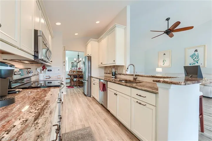 Kitchen featuring a sink, a ceiling fan, stone countertops, appliances with stainless steel finishes, and a peninsula