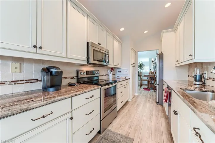 Kitchen with light wood finished floors, light stone countertops, stainless steel appliances, white cabinetry, and a sink
