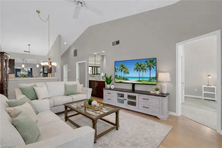 Living area featuring high vaulted ceiling, light wood finished floors, a ceiling fan, and a chandelier