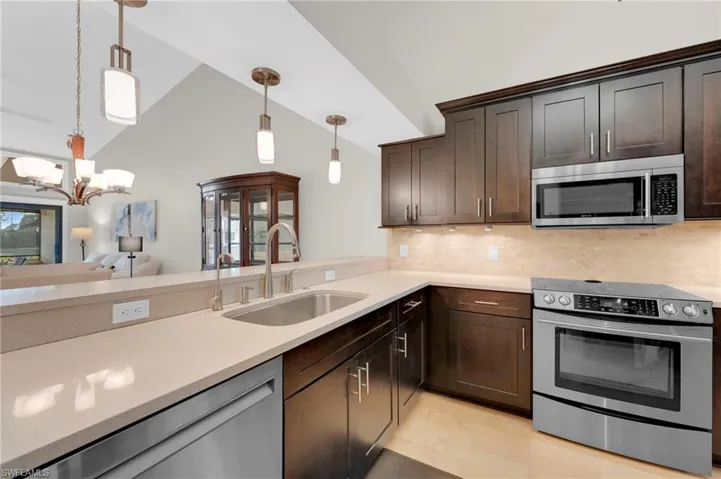 Kitchen featuring appliances with stainless steel finishes, lofted ceiling, light wood-style floors, dark brown cabinetry, and decorative light fixtures