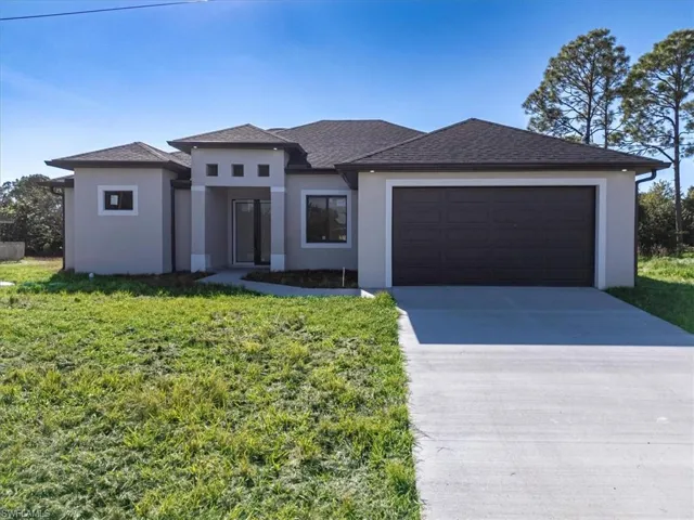 Prairie-style house with an attached garage, concrete driveway, stucco siding, a front lawn, and roof with shingles