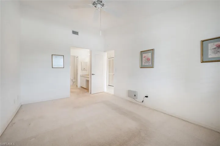 Empty room with ceiling fan, light colored carpet, and a high ceiling