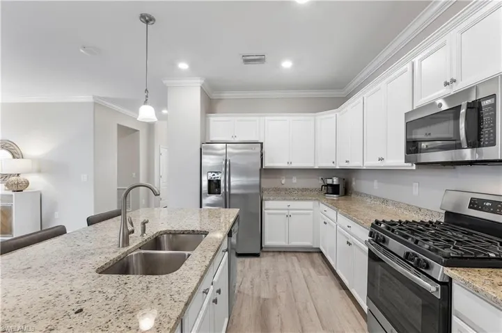 Kitchen featuring ornamental molding, stainless steel appliances, sink, white cabinets, and light hardwood / wood-style flooring
