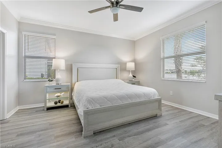 Wake to the expansive lake views in the Primary Bedroom with multiple windows, ceiling fan, and light hardwood / wood-style flooring