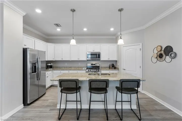Kitchen with white cabinets, appliances with stainless steel finishes, a kitchen island with sink, and light hardwood / wood-style floors
