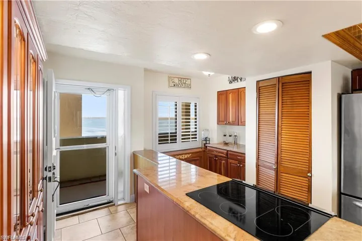 Kitchen with brown cabinets, freestanding refrigerator, recessed lighting, light tile patterned floors, and cooktop