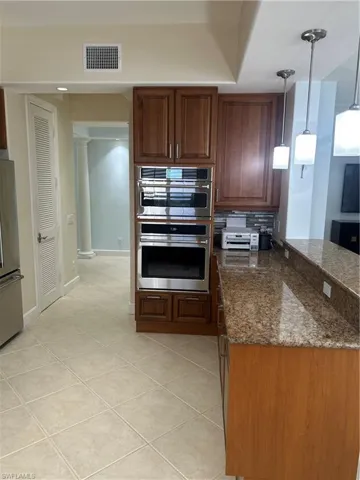Kitchen featuring double oven, dark stone countertops, fridge, light tile patterned flooring, and hanging light fixtures