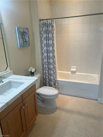 Bathroom featuring shower / bathtub combination with curtain, vanity, and light tile patterned floors