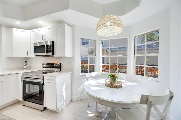 Kitchen with appliances with stainless steel finishes, white cabinets, pendant lighting, and light stone countertops