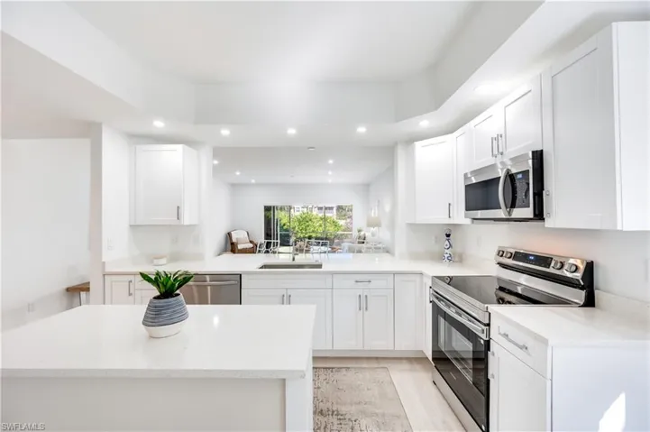 Kitchen with appliances with stainless steel finishes, white cabinets, light stone countertops, and recessed lighting