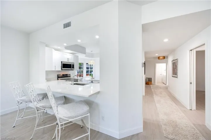 Kitchen with light stone countertops, white cabinets, light wood-style flooring, a kitchen bar, and recessed lighting