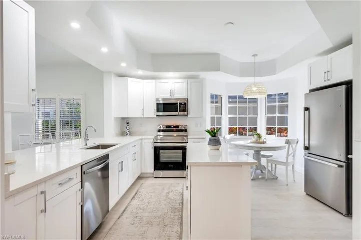 Kitchen with stainless steel appliances, light stone countertops, pendant lighting, white cabinetry, and a kitchen island