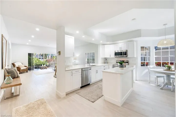 Kitchen with open floor plan, white cabinets, a kitchen island, stainless steel appliances, and decorative light fixtures