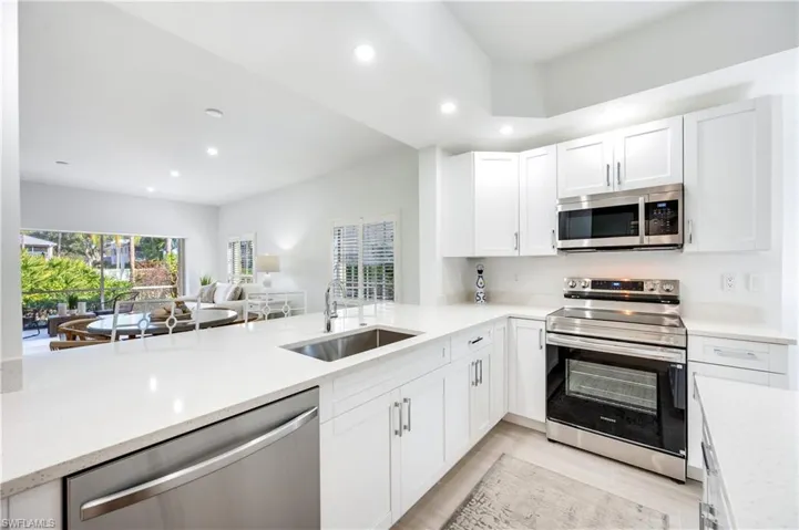 Kitchen featuring appliances with stainless steel finishes, white cabinetry, recessed lighting, light stone countertops, and open floor plan