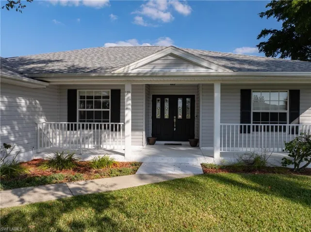 Doorway to property featuring a porch, roof with shingles, and a yard