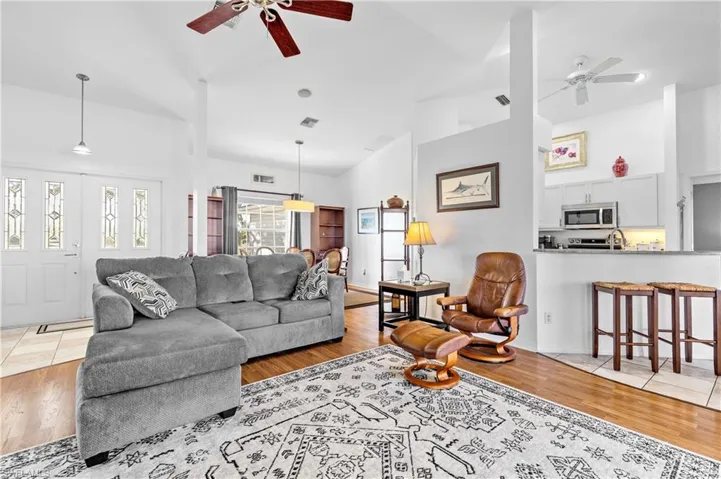 Living area featuring ceiling fan, high vaulted ceiling, and light wood-style flooring