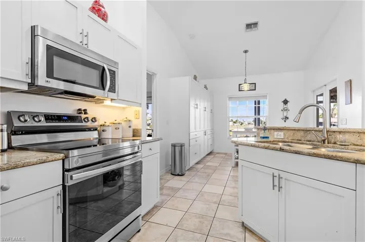 Kitchen with stainless steel appliances, white cabinetry, light stone counters, and lofted ceiling
