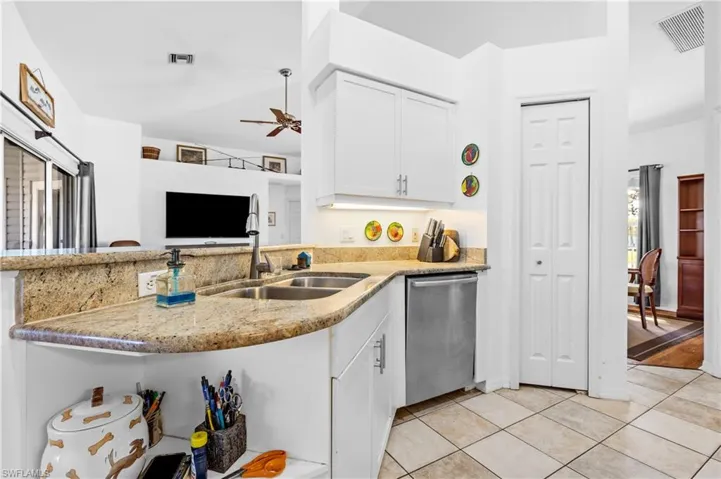 Kitchen with white cabinets, dishwasher, light stone counters, light tile patterned floors, and open floor plan
