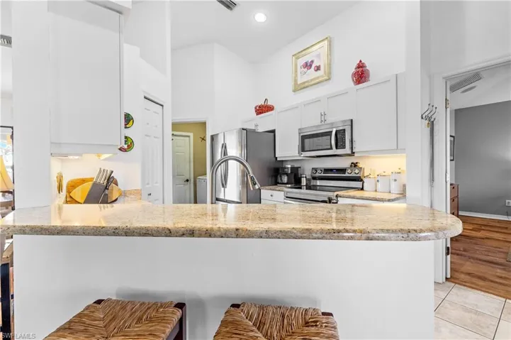 Kitchen with a peninsula, a kitchen breakfast bar, white cabinets, light stone countertops, and a towering ceiling