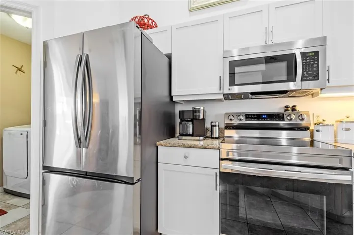 Kitchen featuring stainless steel appliances, white cabinetry, light stone countertops, and tile patterned floors