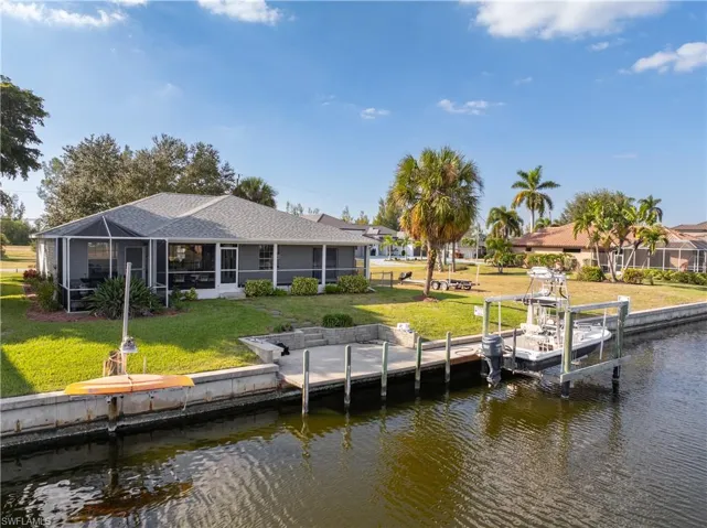 Back of property featuring a sunroom, a lawn, boat lift, a lanai, and a water view
