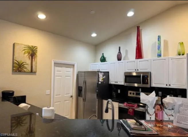 Kitchen featuring vaulted ceiling, white cabinetry, stainless steel appliances, dark countertops, and recessed lighting