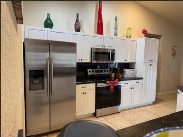 Kitchen featuring stainless steel appliances, dark countertops, lofted ceiling, white cabinetry, and light tile patterned floors