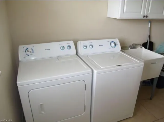 Laundry room featuring washing machine and clothes dryer, cabinet space, a sink, and light tile patterned floors
