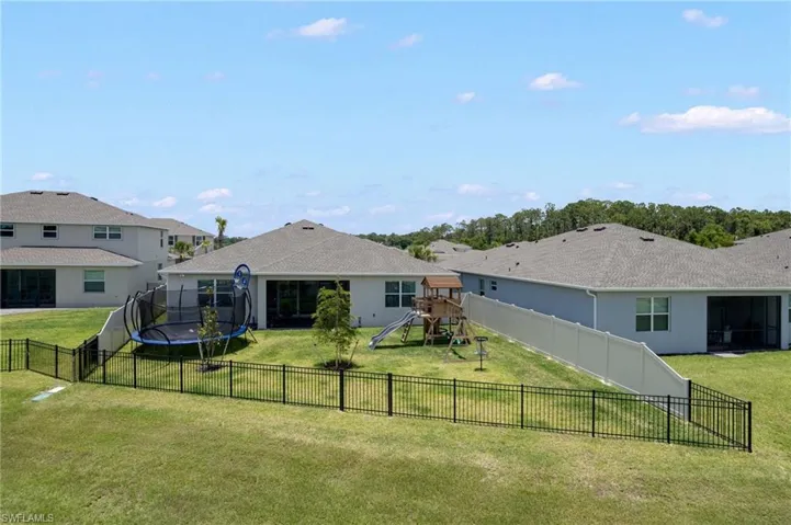 Expansive backyard featuring a black metal fence, mature trees, and a screened lanai