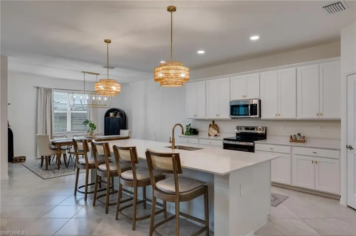 Spacious kitchen featuring an expansive island with seating, white shaker cabinetry, stainless steel appliances, and light-toned tile flooring