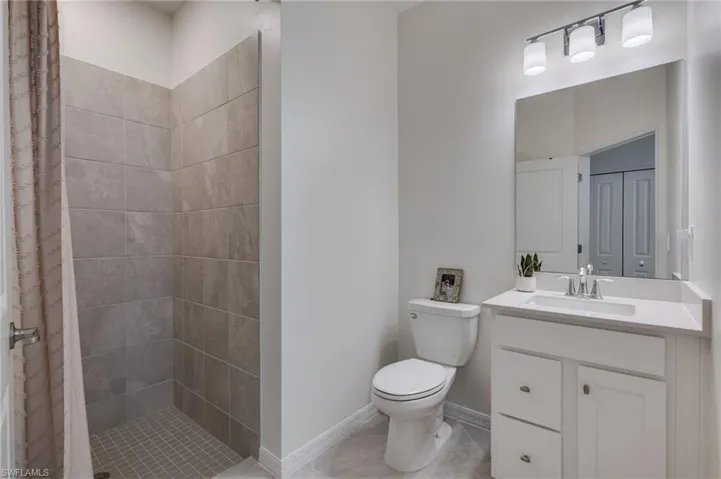 Bathroom featuring a tiled standing shower, white vanity with integrated sink, chrome faucet, and a large wall-mounted mirror