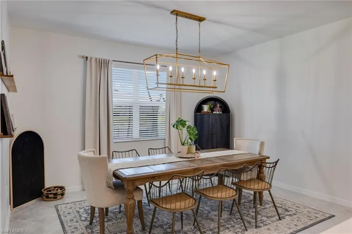 Dining area featuring a contemporary gold-finished rectangular chandelier, a window with horizontal blinds, and light-toned flooring