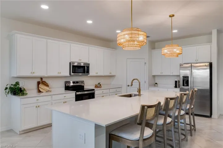 Spacious kitchen featuring an expansive island with seating, white shaker-style cabinetry, stainless steel appliances, and two decorative pendant lights