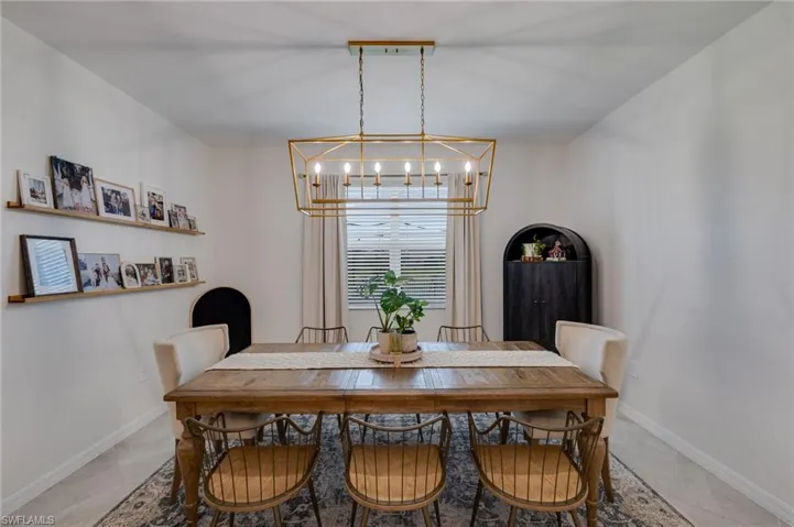 Dedicated dining space featuring a gold-finish geometric chandelier, window with blinds and drapes, and light-toned flooring