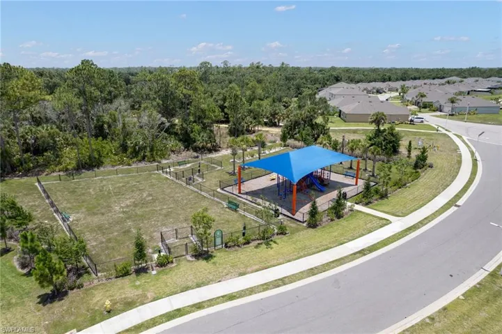 Recreational area featuring a fenced pet park and a shaded playground structure with slides and benches
