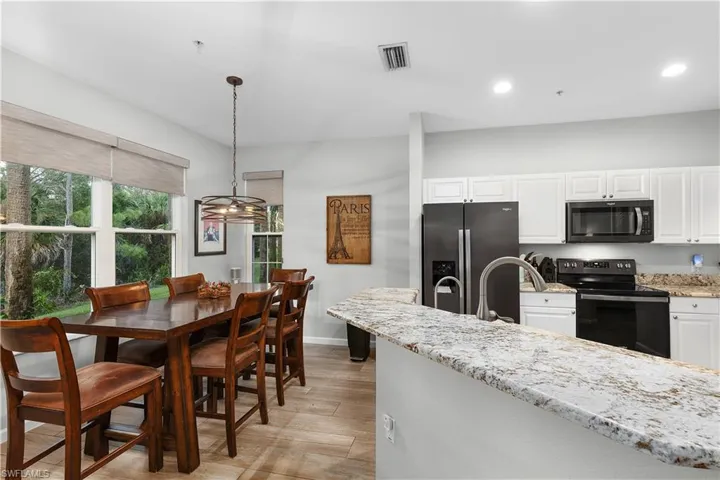 Kitchen with light stone countertops, black appliances, decorative light fixtures, light hardwood / wood-style flooring, and white cabinets