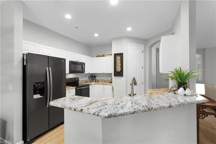 Kitchen featuring white cabinetry, black appliances, light stone counters, and light wood-type flooring