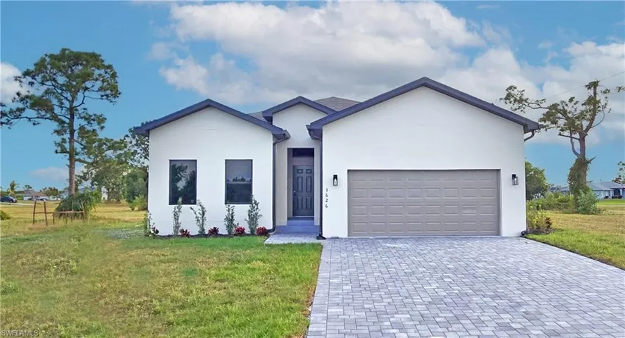 Ranch-style home with decorative driveway, a front yard, an attached garage, and stucco siding
