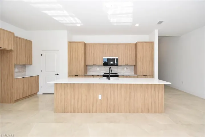 Kitchen with backsplash, a center island with sink, black microwave, and modern cabinets