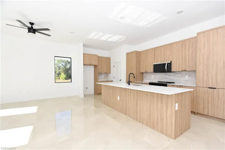 Kitchen featuring modern cabinets, tasteful backsplash, an island with sink, light stone counters, and stainless steel microwave
