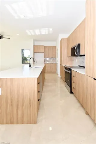 Kitchen with modern cabinets, range with electric cooktop, stainless steel microwave, light stone counters, and backsplash