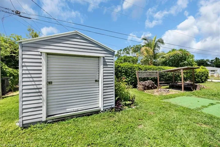 Detached storage shed with roll-up door, expansive green lawn, and privacy hedging