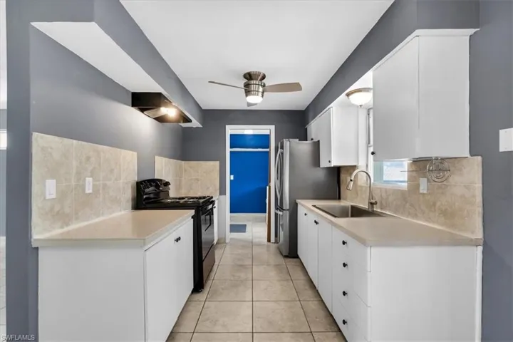 Galley-style kitchen with white cabinetry, light-toned countertops, and a tile backsplash