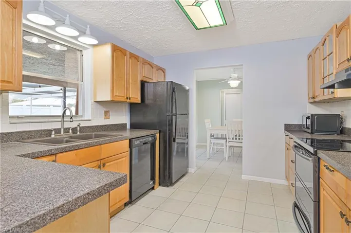 Kitchen featuring black appliances, backsplash, a textured ceiling, light tile patterned floors, and ceiling fan